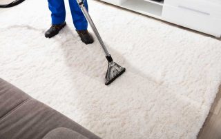 This image shows a man using a vacuum to clean a carpet. The carpet being cleaned is color white.