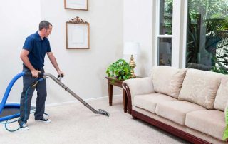 This image shows a man using a vacuum to clean a carpet. The carpet being cleaned is color white.